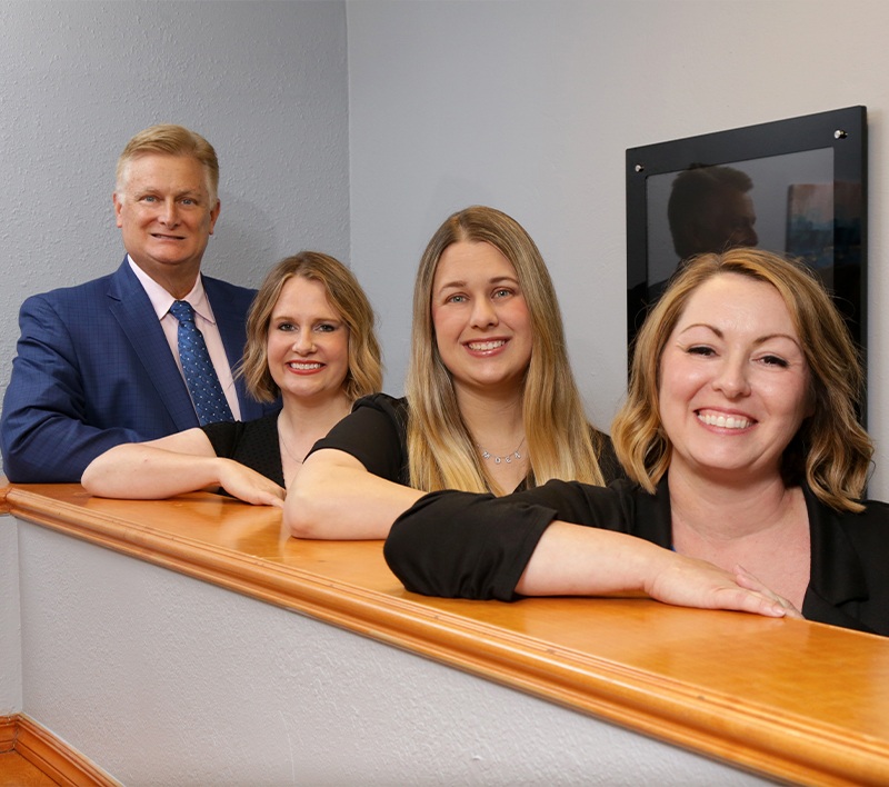 Edmond Oklahoma dentist and three dental team members leaning against wooden counter