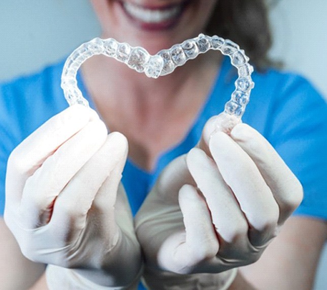 dental team member holding two clear aligners in the shape of a heart
