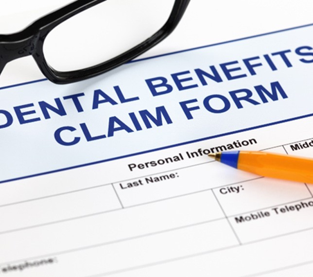 A dental benefits claim form with pen and glasses
